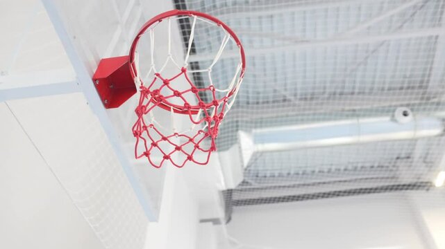 Professional-grade basketball rim stands firm in modern school sports hall. Sunlight streams through high windows onto gleaming backboard