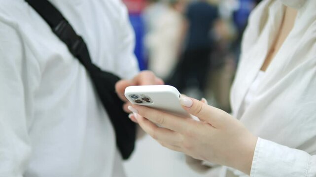 Man and a woman are looking at a cell phone. The man is holding a black bag and the woman is wearing a white shirt