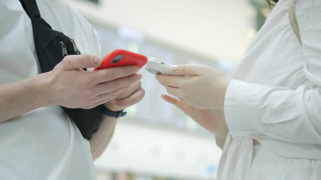 Two people are talking on their cell phones in a public place. One of them is holding a white card
