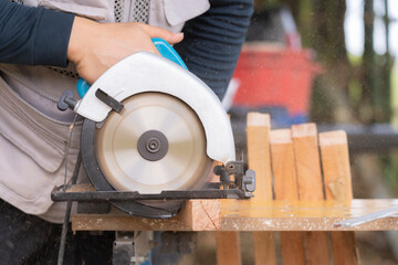 Carpenter cutting wood with electric circular saw, woodworking and craftsmanship concept