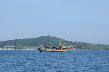 Obraz premium Fishing boat at sea near a lush green island on a sunny day