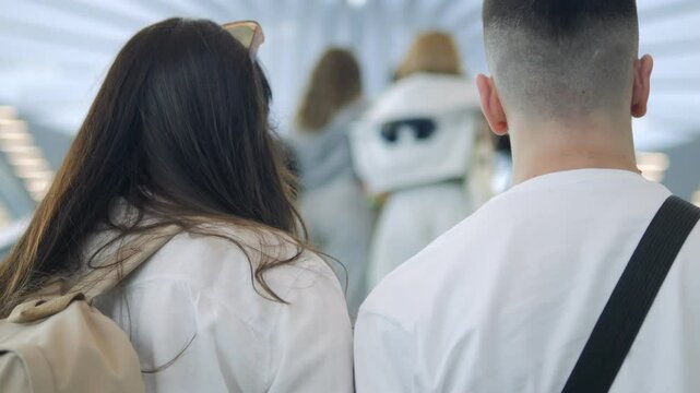 Man and a woman are walking together in a subway station. The woman is wearing a white shirt and a backpack. Scene is casual and relaxed