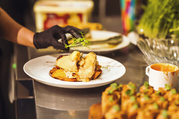 Close-up of a chef garnishing a creamy gourmet dish with microgreens in a professional kitchen, highlighting precision, creativity, and modern food presentation.