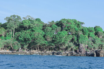 Lush green tropical island shoreline with rocky coastline and calm ocean water