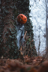 Spooky scarecrow with carved pumpkin head and axe in hand hides in misty autumn forest. Halloween concept