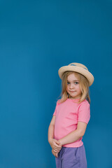 Young child poses against a vibrant blue wall wearing a straw hat and bright clothing