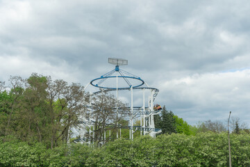 Thrilling Amusement Park Ride Soaring Above Lush Green Trees Under A Bright Sky. Exciting Adventure...
