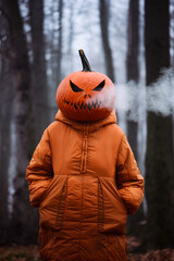 Halloween girl in spooky pumpkin head with smoke coming out of her mouth in the misty autumn forest. Scary woodland moment filled with mystery, costume play, and autumn mood