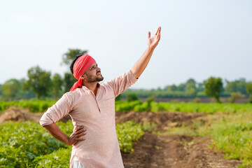 young indian farmer standing at green agricultural field