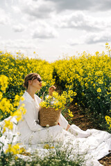 Woman sits among vibrant yellow flowers while holding a basket on a sunny day