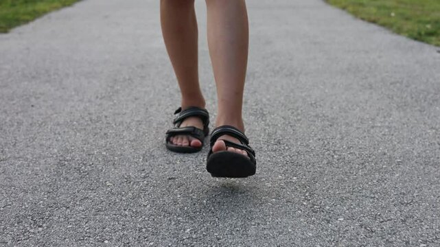 Close-up child feet in sandal waking om asphalt pathway in park