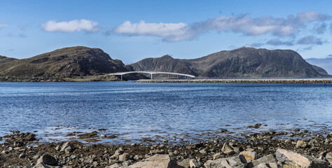 Scenic Coastal Road Bridge Next to Calm Waters and Rocky Terrain Under Cloudy Sky, Runde, Norway