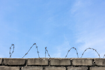 Brick wall topped with rusty barbed wire against clear blue sky.