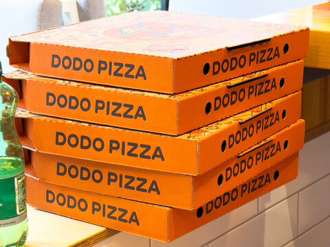 Ljubljana, Slovenia - June 03, 2025: Stacked Dodo Pizza boxes in vibrant orange color on a wooden table, showcasing the brand's unique packaging and inviting atmosphere for pizza lovers