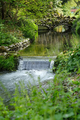 Small waterfall in the garden with stone bridge in the background, England