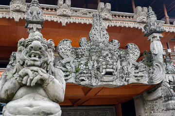 Close-up of a Balinese guardian statue and elaborately carved temple gate at a traditional building...