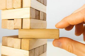 Stacking the Odds: A hand delicately maneuvers a wooden block within a precarious tower of similar blocks, emphasizing the balance and strategic thinking. 
