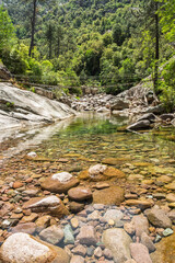 Steel rope bridge crossing the crystal clear pools and rocks of the Figarella river at Bonifatu oin the Balagne region of the Mediterranean island of Corsica