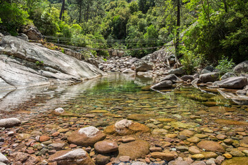 Steel rope bridge crossing the crystal clear pools and rocks of the Figarella river at Bonifatu oin the Balagne region of the Mediterranean island of Corsica