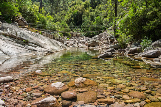 Steel rope bridge crossing the crystal clear pools and rocks of the Figarella river at Bonifatu oin the Balagne region of the Mediterranean island of Corsica