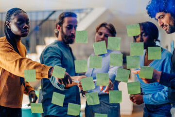 Businesspeople planning strategy using adhesive notes on glass wall in office