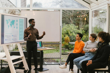 Young businessman presenting global marketing strategy to colleagues in modern office