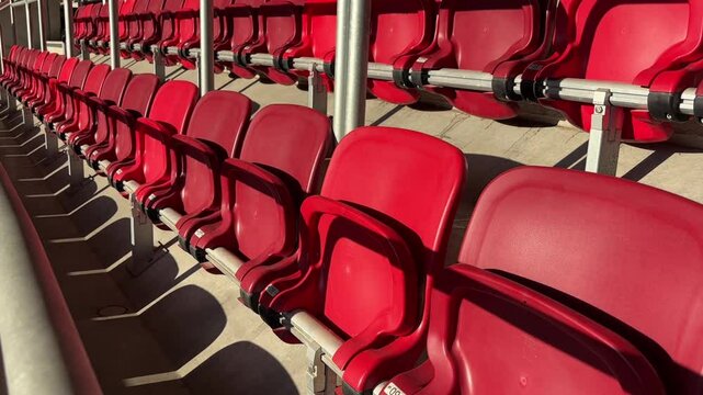 Rows of bright red plastic stadium chairs in sunlight, ready to welcome sports fans and event spectators. 
