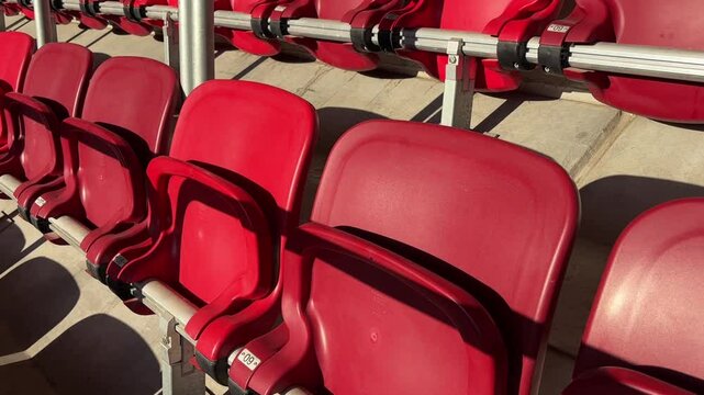 Rows of bright red plastic stadium chairs in sunlight, ready to welcome sports fans and event spectators. 