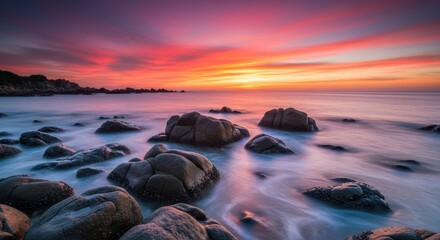 Naklejka premium Rocks Meet Sea Under Brilliant Sunset Sky
