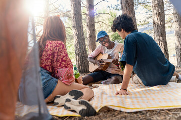 Happy diverse friends singing and playing acoustic guitar together at a campsite in a forest