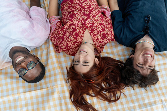Happy diverse friends lying in a circle on a picnic blanket, smiling together in a park. - Powered by Adobe