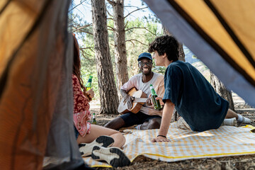 Diverse friends enjoying music and conversation, playing acoustic guitar at a campsite