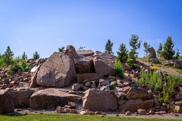 hill of rocks, stones, and boulders with a few coniferous trees under a blue sky in the summer