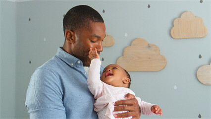 Father Cuddling Baby Daughter In Nursery Decorated With Clouds
