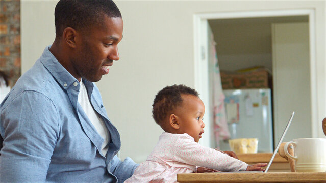 Father Holding Baby Daughter Playing With Laptop At Home