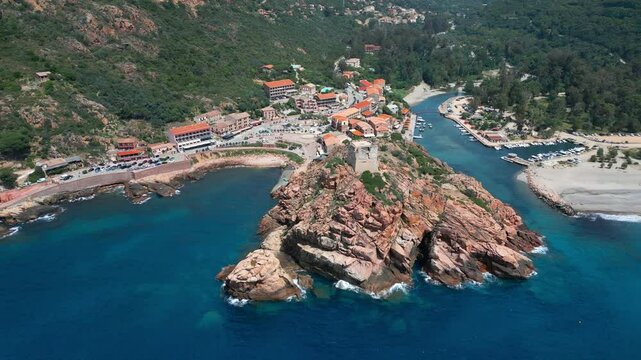 Aerial view circling the Genoise tower on a rocky outcrop, the beach and town of Porto on the west coast of the Mediterranean island of Corsica with mountains behind