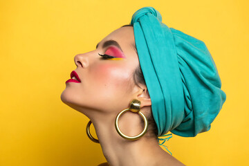 Woman in teal turban with bold makeup and gold hoops