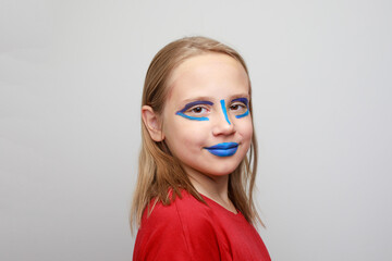 Happy girl child with vibrant blue and red face paint makeup on her cheeks and forehead. Halloween...