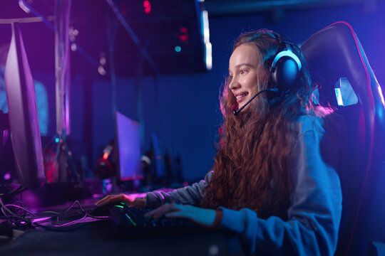 Young caucasian woman streaming video games with enthusiasm in neon lit gaming setup
