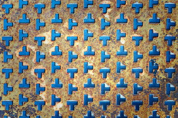 Rusted metal diamond plate with a repeating raised T-shaped embossed pattern. Industrial background...