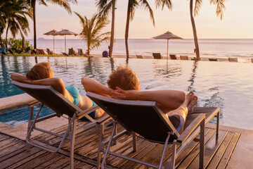 couple on holidays trip, romantic vacation in luxury beach hotel sitting near swimming pool at sunset