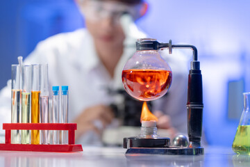 Scientific experiment heating a red chemical liquid in a Florence flask over an alcohol burner in a research lab.