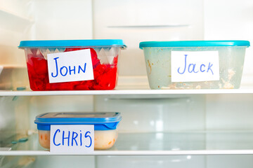 Office lunch containers with handwritten name stickers in shared fridge. Healthy food preparation for work office study.