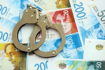 Israel New Shekels banknotes and handcuffs. The current Israel money bills and cuffs lies on table...