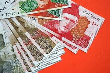Pakistan rupees banknotes on red background. The current Pakistan money bills lies on table in big...