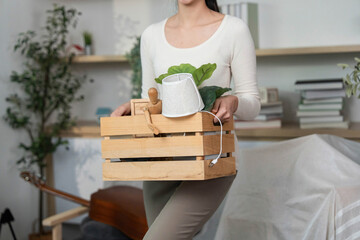 Moving Essentials. Woman holding a crate with plants and decor items during relocation.