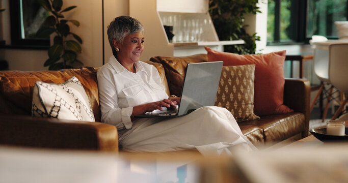 Mature woman, laptop and typing on sofa with smile for project, ebook and creativity for novel. Person, writer and author with computer on couch, happy and editing process in lounge at apartment - Powered by Adobe