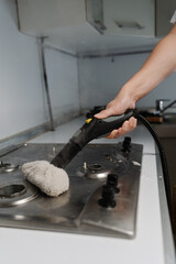 Vertical shot of man cleaning dirty gas stove using steam cleaner and cloth, removing grease and...