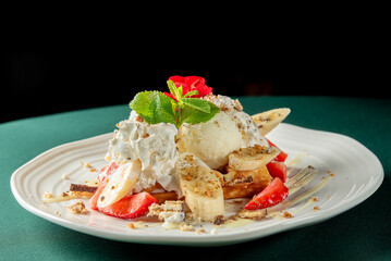 Waffles topped with vanilla ice cream, whipped cream, banana slices, strawberries, mint, and a red...