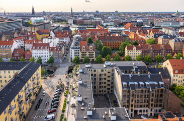 Panoramic view of Copenhagen taken from the top of the Church of Our Saviour, showing a mix of historical rooftops, modern buildings, and city landmarks under a warm evening sky.